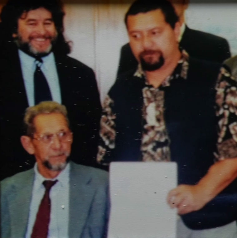 Three men, one of whom is Pootanga Neilson holding a piece of paper.