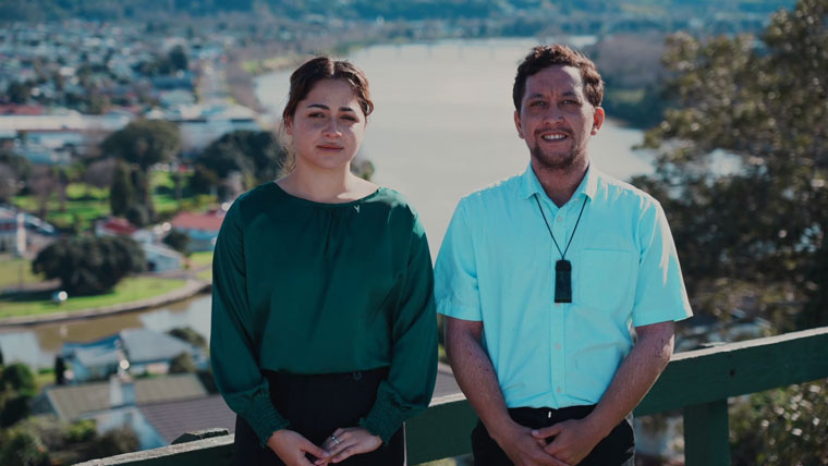 A man and a woman standing on a hill above a river facing the camera.