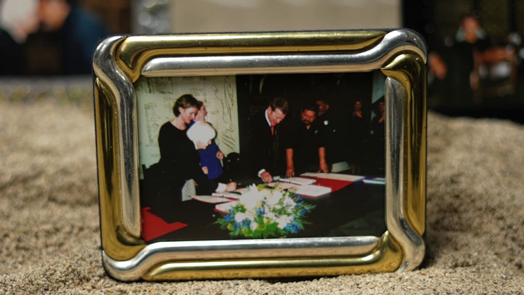 A gold photoframe with a photograph of three people signing the Ngaa Rauru Kiitahi Deed of Settlement