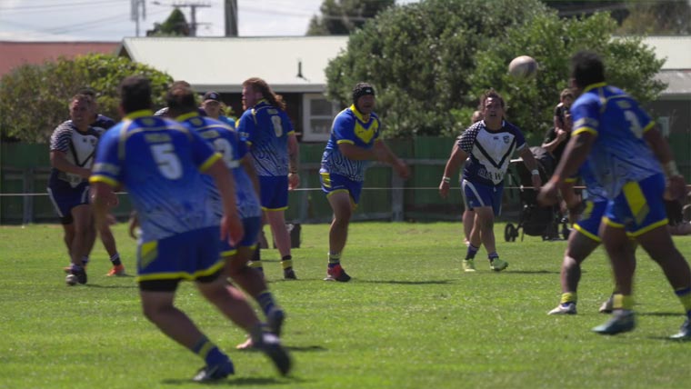 Rugby players mid tackle, one team is in blue the other in white.