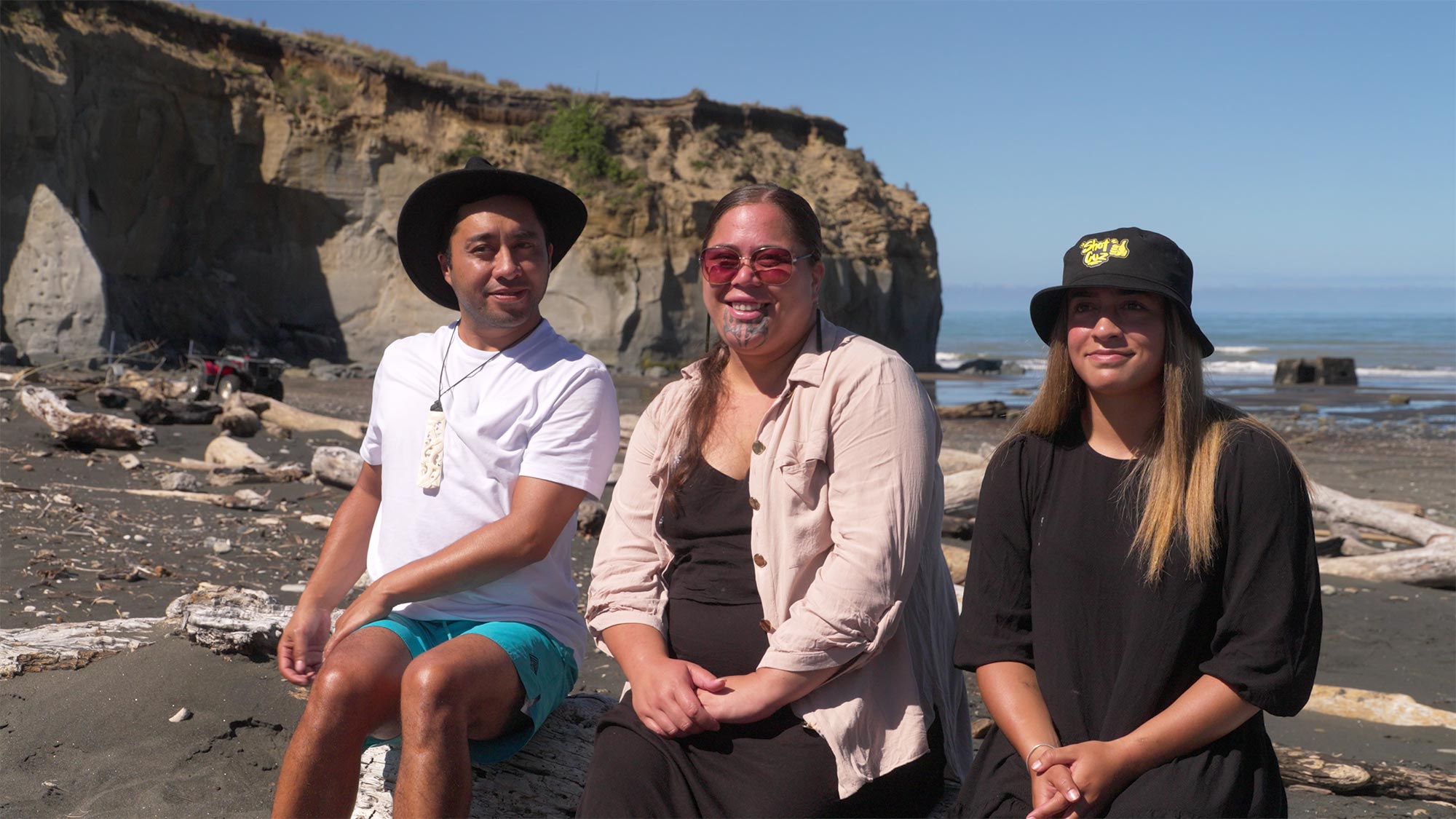 Two women and a man sat on a rock at Kai Iwi beach.
