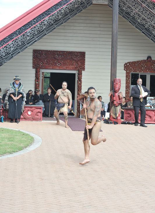 He kaiwero e pekepeke haere ana ki mua ki te wharenui; kei muri tonu ko ētahi anō tāngata e whanga ana