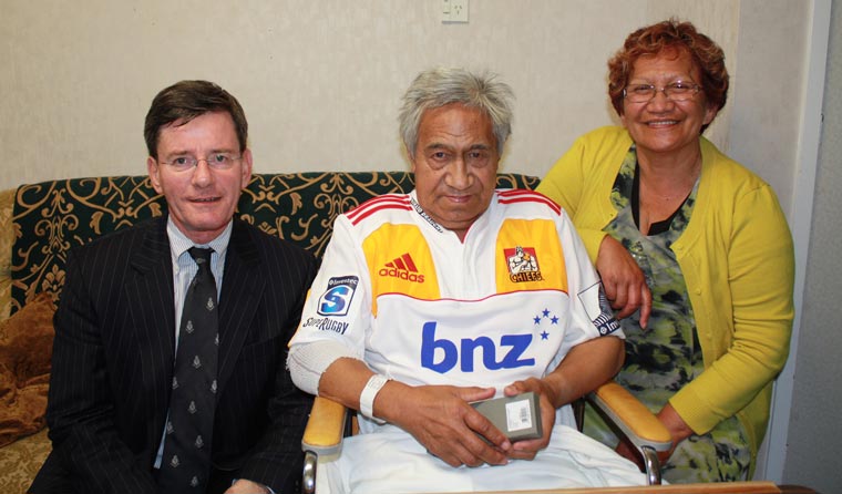 Man in suit sitting next to man in wheelchair and Chief's shirt and a woman in a yellow cardigan.