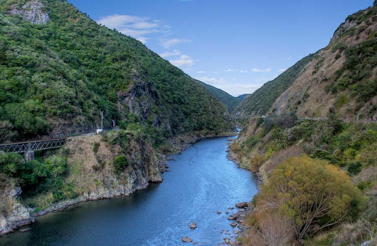 River running through a gorge with railway line and bridge on one side and road on the other.