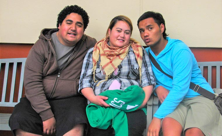 Two young men on either side of a young woman on a bench.