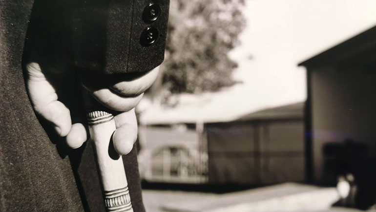 Close-up image of a hand on a walking stick with buildings in the background
