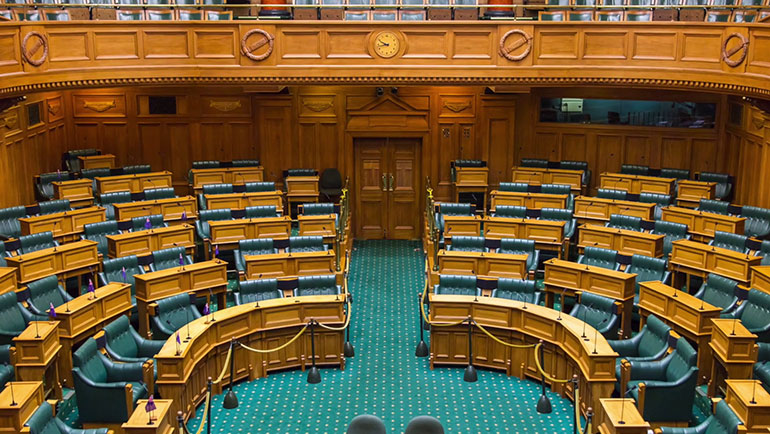 Inside the Debating Chamber with wooden desks and paneling and green carpet and seats  