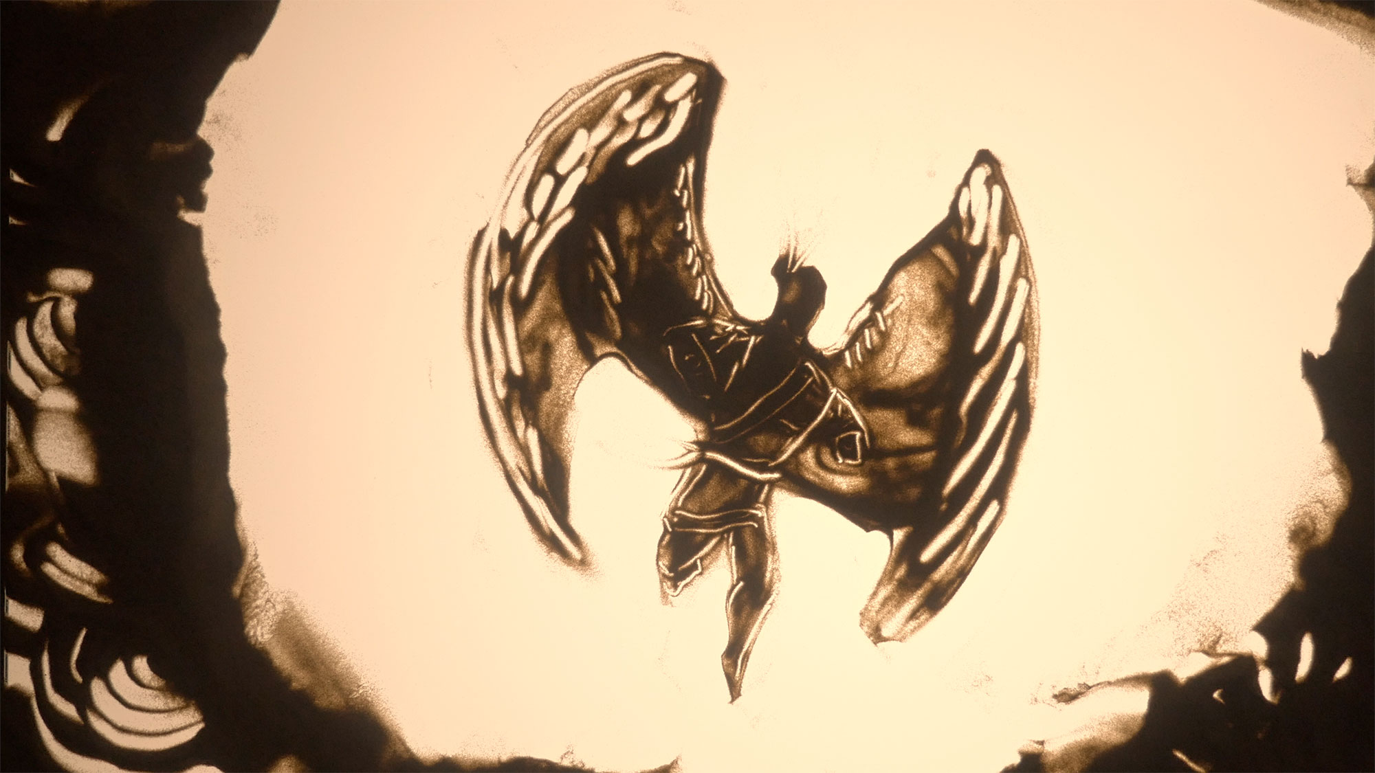 A figure with wings drawn out of sand on a lightbox.